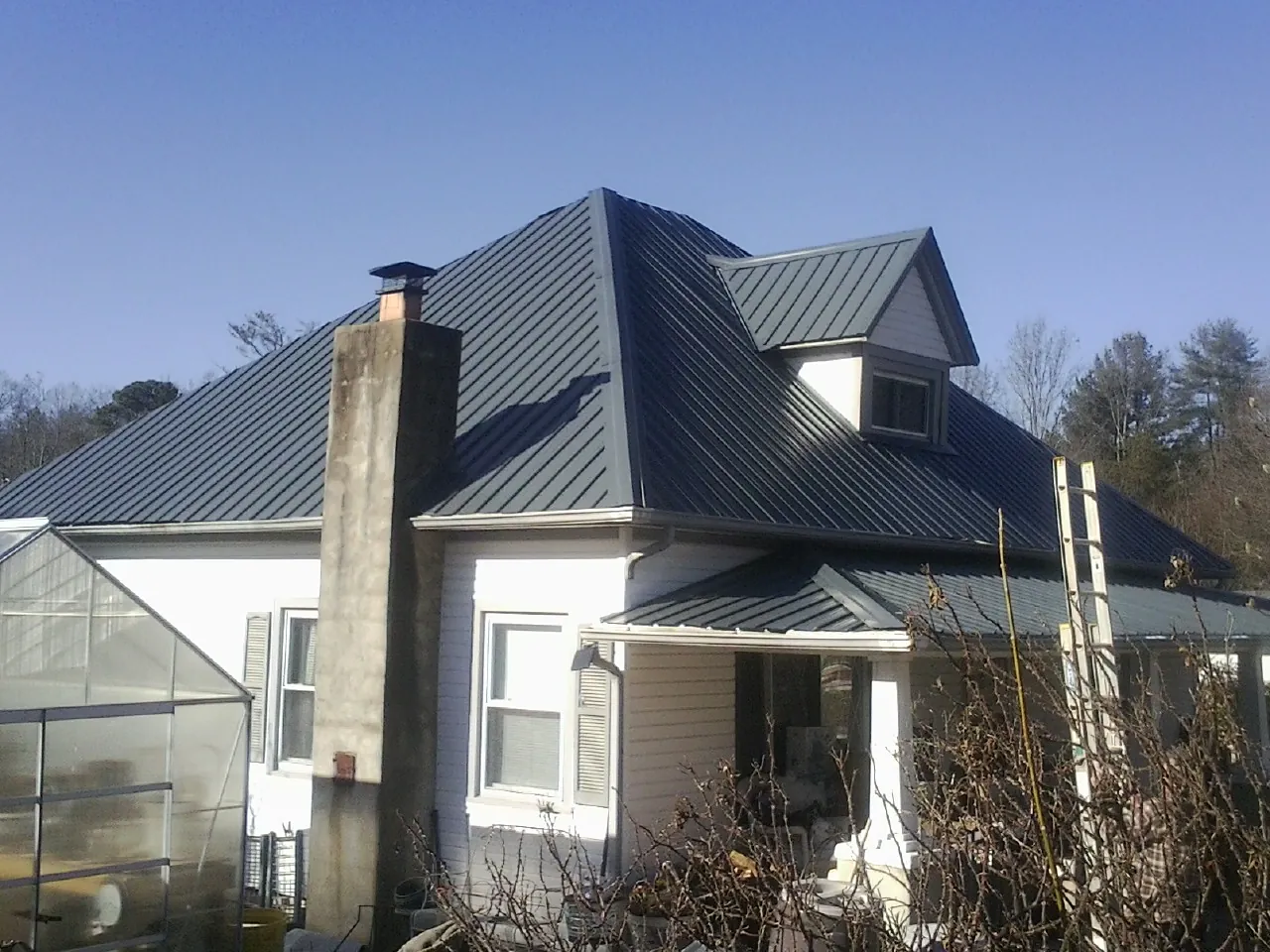 Dark blue standing seam metal roof on a white farmhouse with dormer — Slate & Tile Roof Repair by Roofing Brothers in North Arlington