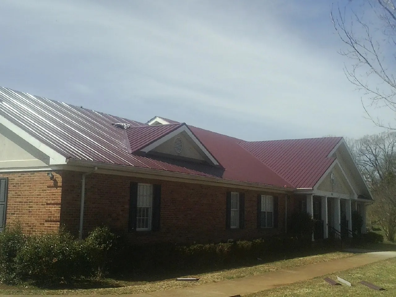 Red metal roof with gabled entries on a long brick building, from a Hail Damage Roof Repair job in North Arlington