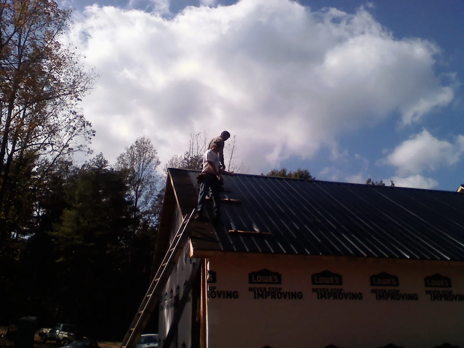Roofer fastening dark metal panels high against a cloudy sky, from a Roof Inspection job in North Arlington
