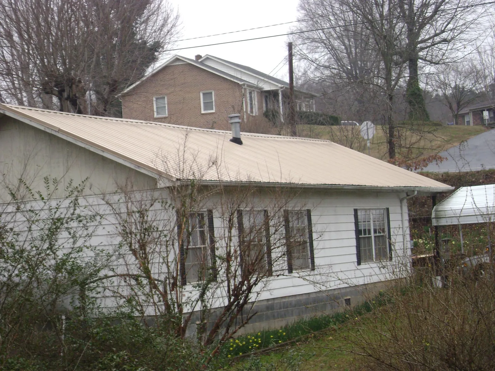 Tan metal roof on a white sided house set into a hillside — Commercial Roofing by Roofing Brothers in North Arlington